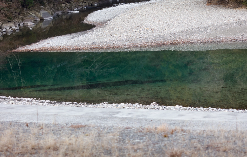 A dark green river cuts betweeen two gray pebble-y banks.