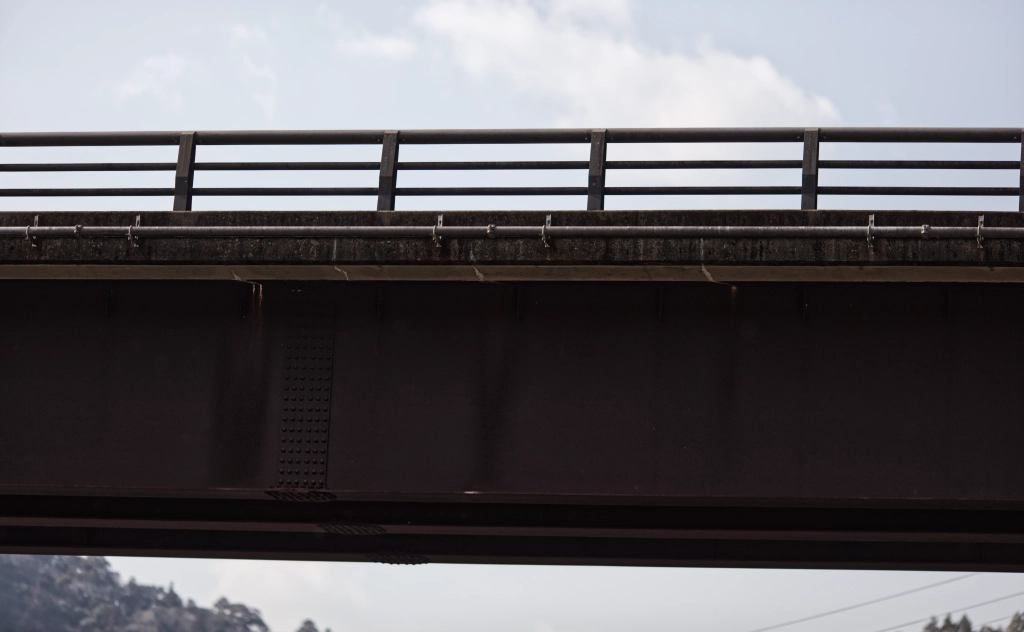 A dark brown metal bridge w/ trailing cuts between two halves of a blue sky.