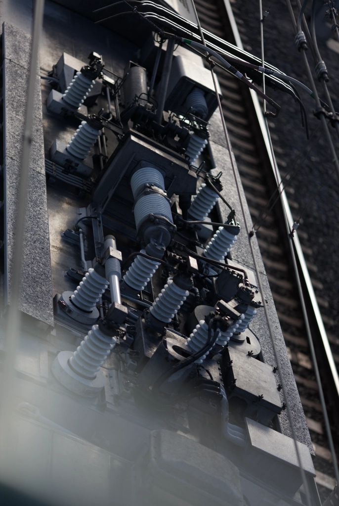 The contours of stacked ceramic resistors for a passing train's pantograph are highlighted by a metalic sunlight.