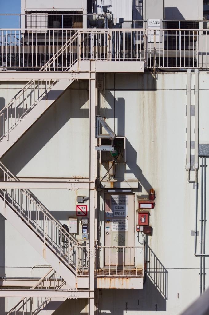 Three flights of fire escape stairs & some rooftop HVAC equipment are viewed from straight-on. The shadows cast are very geometric.