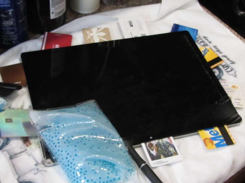 A laptop screen-up on a towel, with a heat pack on the lower left corner, and a plethora of various colorful credit cards and transit cards filling every other gap between the screen and body.