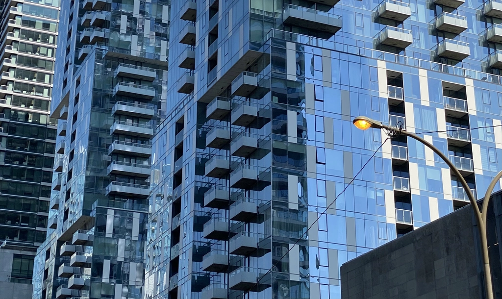 Various up-scale cubic-inspired glass apartment buildings create interesting patterns with their balconies and varying shades of blue tinted glass contrasted against gray paneling. A single old-style light pole pokes out on the right.