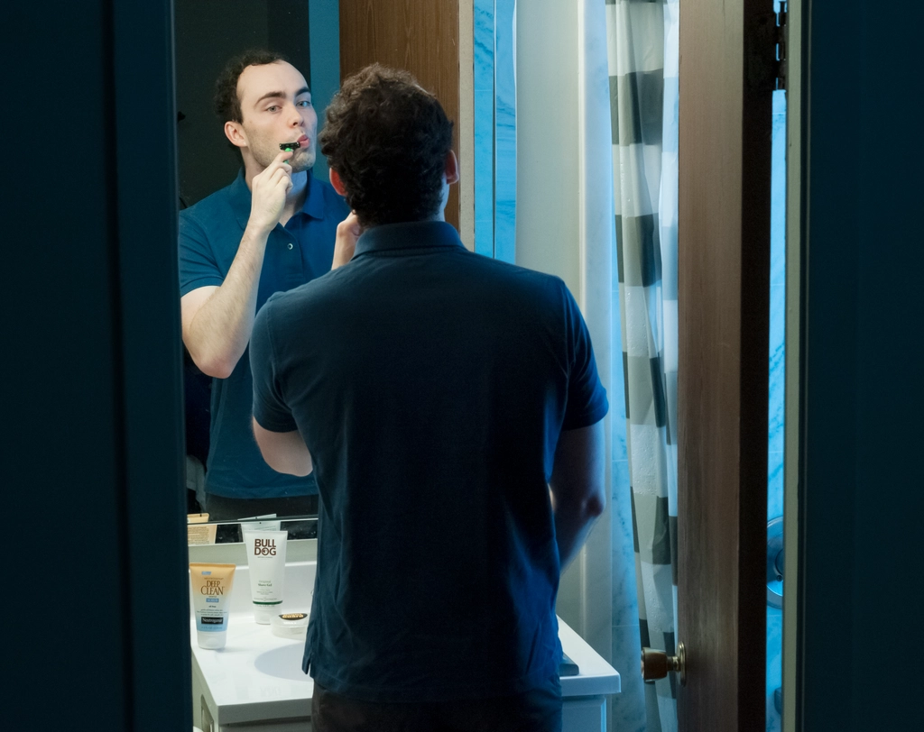 I'm shaving in my bathroom mirror, shot from behind my back over my shoulder from a slightly high angle. The outside of the bathroom is all dark.