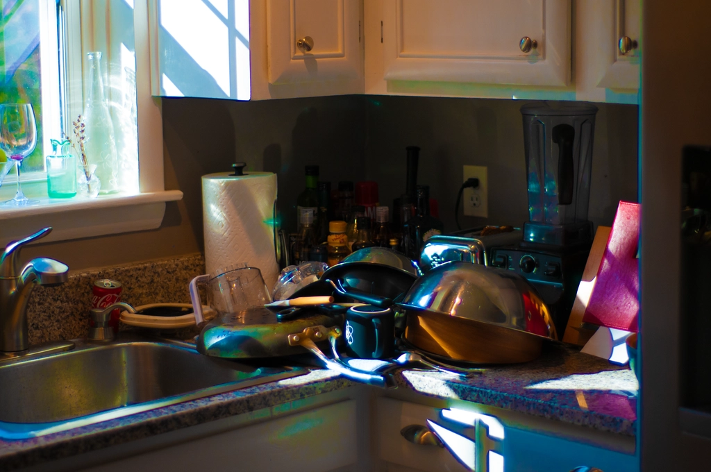 Light from the window reflects off a pile of pans and dishes drying off in a corner of the kitchen. Refraction from the metal pans and reflection from the white cabinets create almost a rainbow of colors throughout the image, interesting lighting conditions.