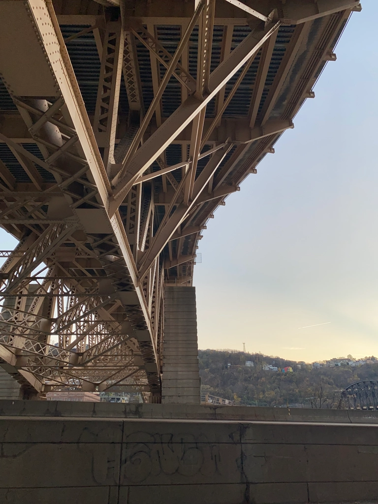 Complex trusses under a wide bridge stretch off into the distance, with the sky a pastel yellow and blue from a low sun.