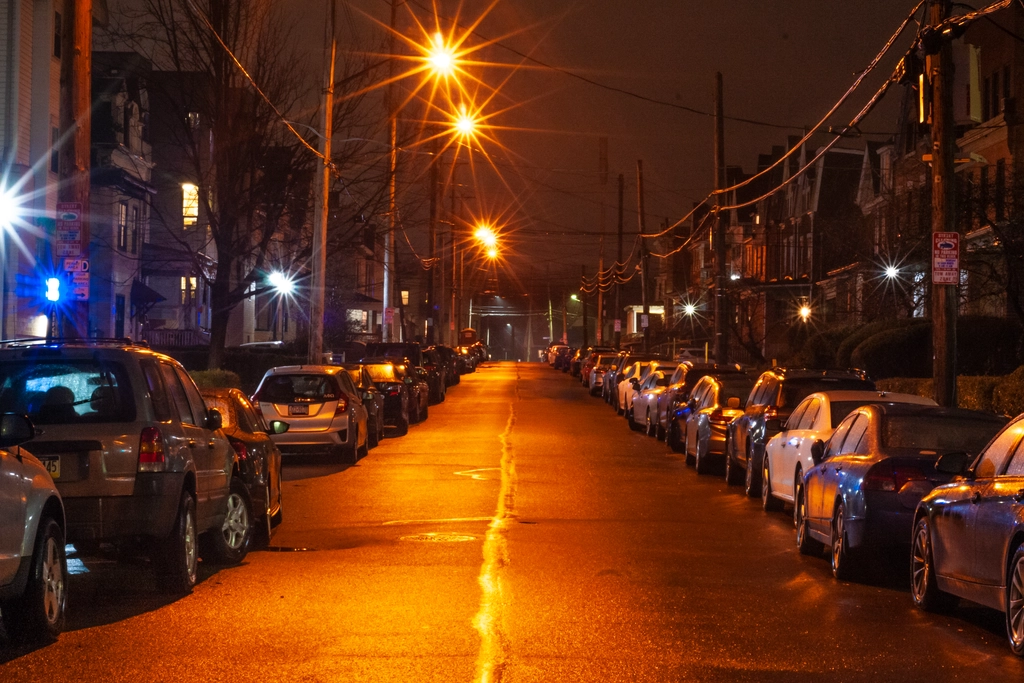 Rows of parked cars bathe under orange sodium lamps. The scene is much brighter than expected, considering it should be night.