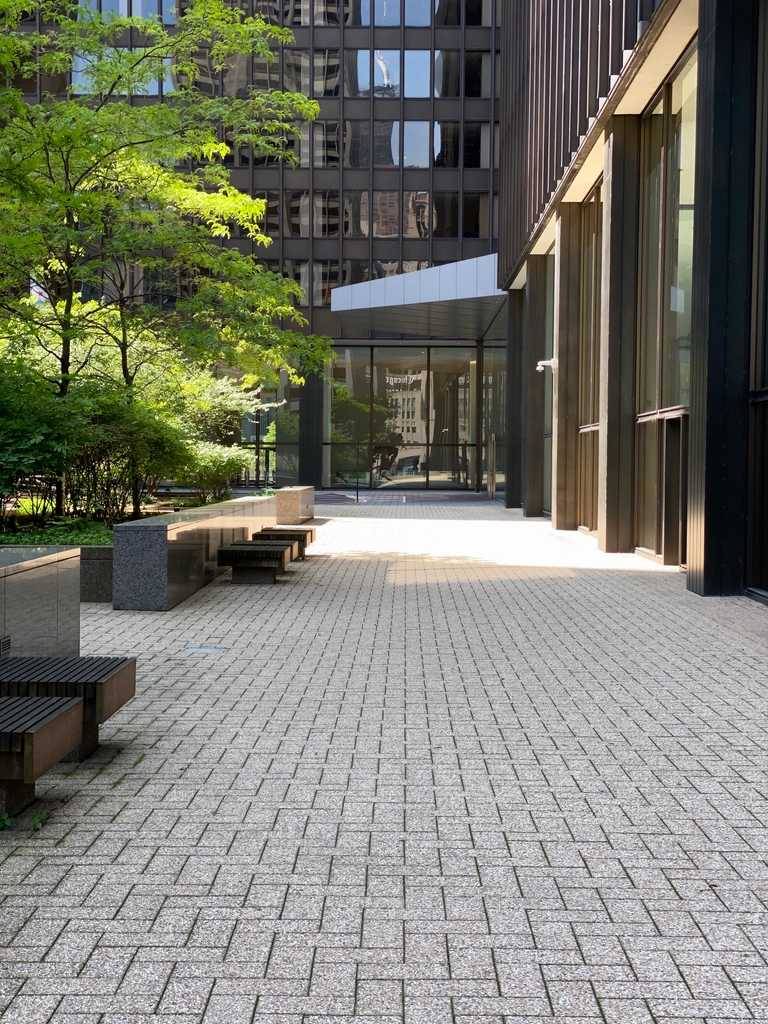 A clean light gray brick courtyard in the morning light, surrounded by dark glass buildings that warp the scenery.