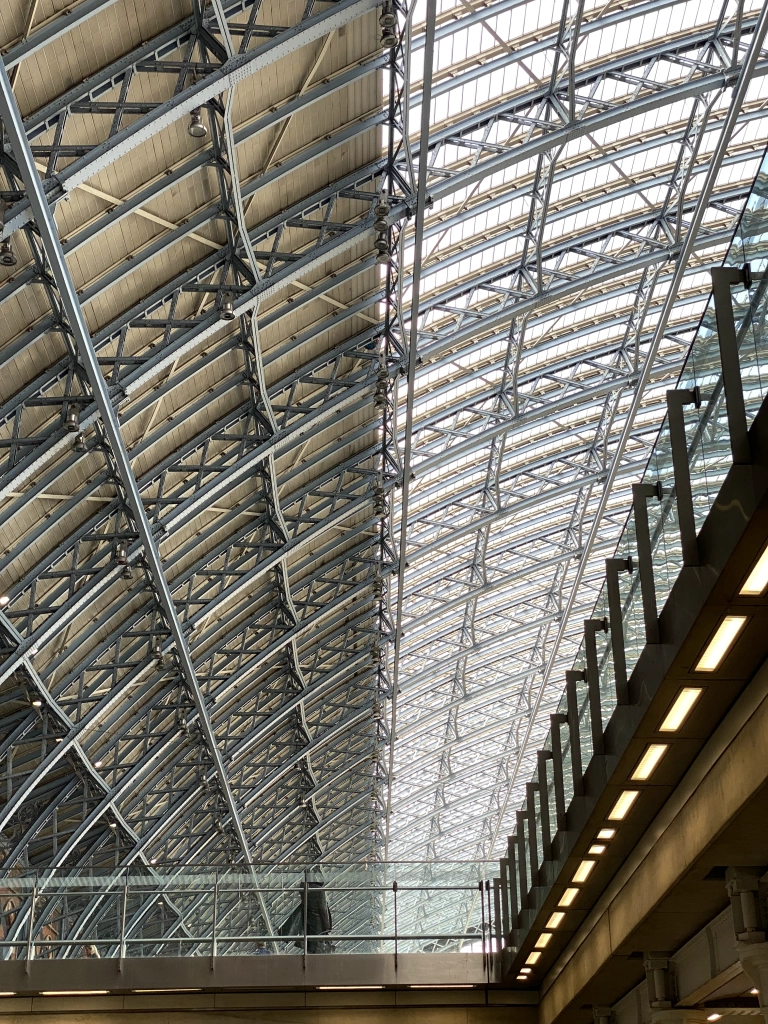 Curved metal beams support an absolutely massive windowed ceiling. Beyond a glass railing, a statue of a man also looks up in wonder.